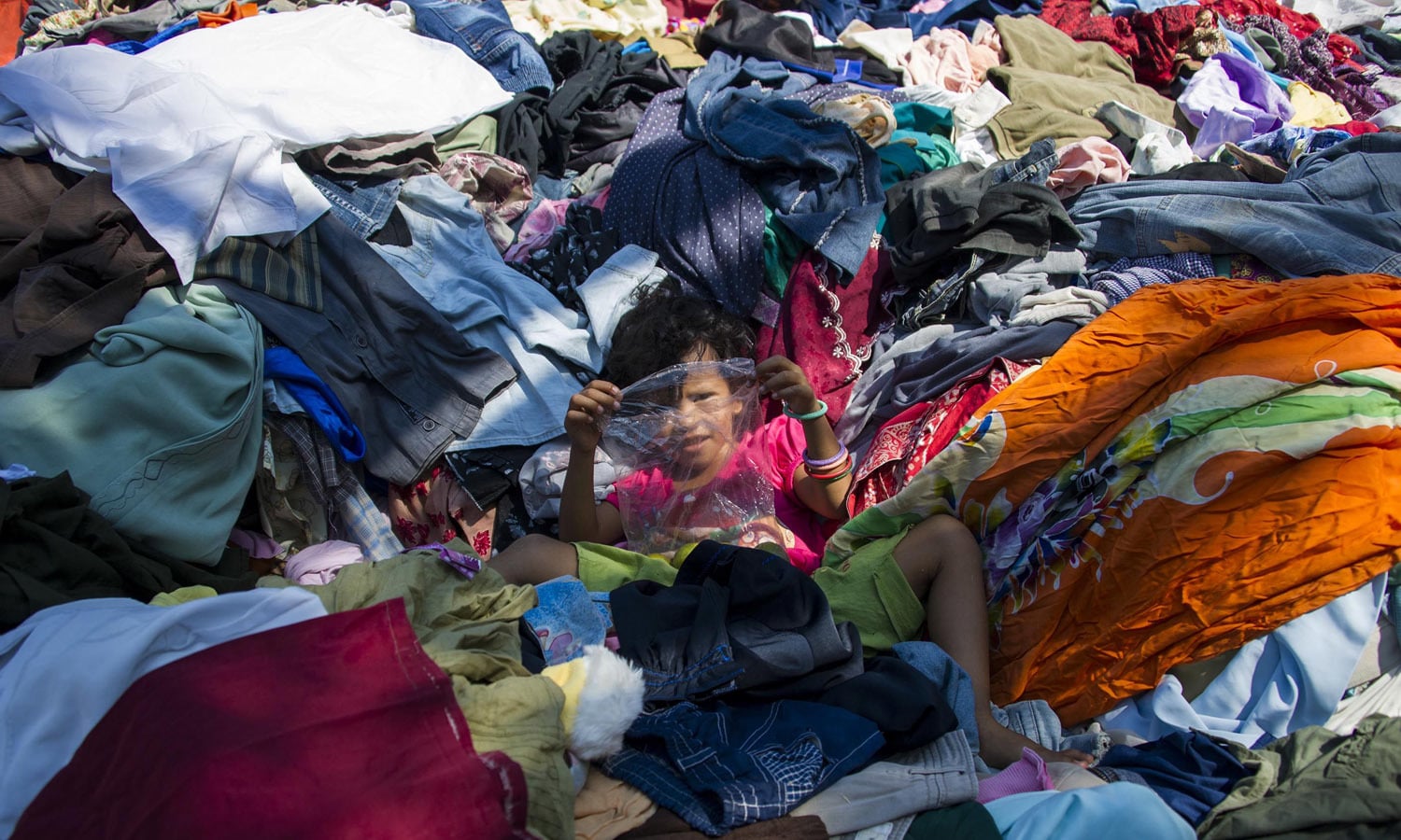 A Rohingya migrant child from Myanmar plays on a pile of clothes donated by Indonesian residents at a confinement — AFP
